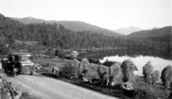 Foto av en bil langs en landevei nær skog og innsjø. Muligen