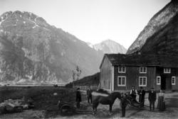 7 personer på et tun med hest og to vogner foran våninghuset