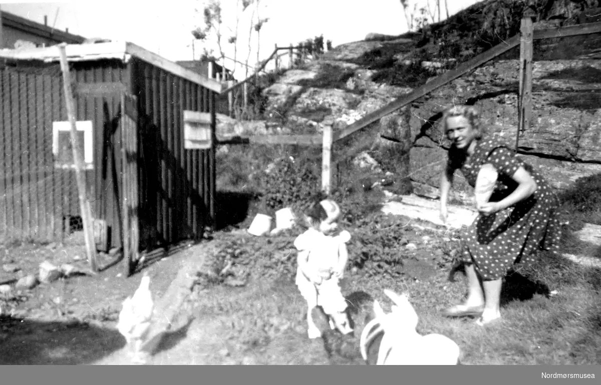 mor og datter forer høner i bakgården, mot utmark og svaberg. Kristiansund ca 1930. Innlandet, Nordlandet? Fra Nordmøre Museum sin fotosamling.