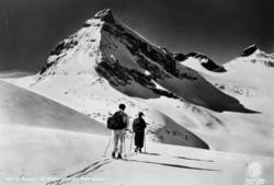 Motiv fra Jotunheimen, hvor vi ser et par på ski en strålend
