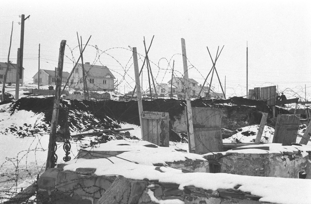Gjenreisning. Ruiner etter krigens ødeleggelser. I bakgrunnen nybygde hus. Bilde ble tatt i Vardø eller Vadsø. Påske 1947.