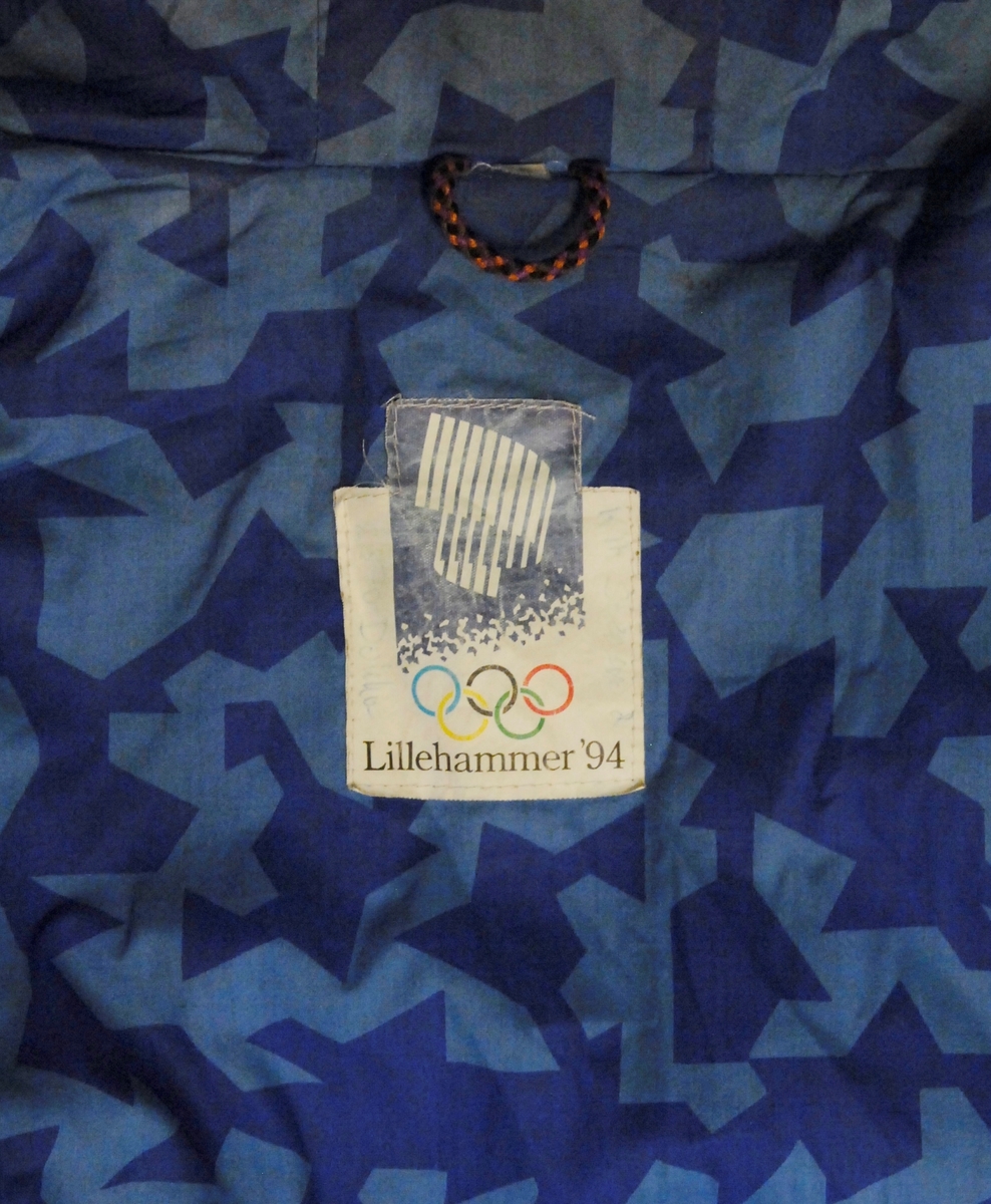 Jakke og nikkers i grå ull med detaljer i skinn. Dressen vart brukt under OL i Albertville 1992 som representasjon for LOOC (Lillehammer Olympiske Organisasjonskomitée). Fóret er i to blåfarger i krystallmønsteret som var ein del av LOOCs designprogram. Logo for Lillehammer 1994 på alle knapper og i skinn på lomme. Brodert "mann med fakkel" foran på jakka. Skinndetaljer på lommer, biser rundt erme, på albue og på kne, og rundt knapper. Ermeopplegg i svart. Hette med avtakbar pelskant.