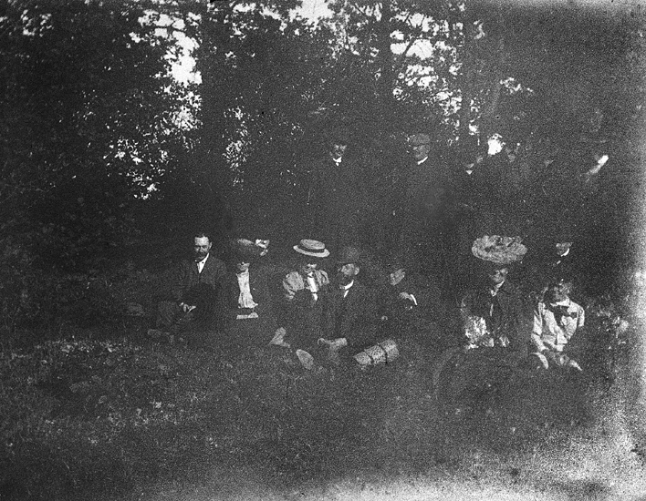 Foto av en grupp människor som slagit sig ner i en skogsglänta.