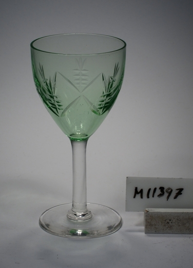 Glas, möjligen vitvinsglas.
Se M 11393 - M 11403, samma servis.
Skärslipad dekor.
Grön kuppa, ben och fot ofärgade. Klarglas.
Ovan angivna mått avser fotdiameter.
Rymd: 10 cl.
Inskrivet i huvudkatalogen 1942.
Funktion: Vitvinsglas