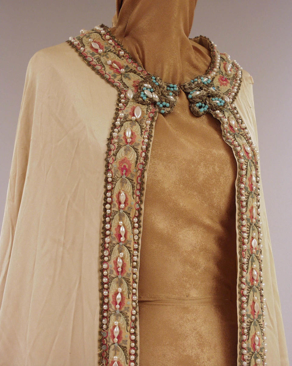 Hvit kappe med detaljer av perler og fargede tråder.
