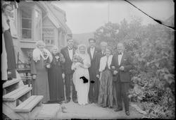 Brudepar med gjester utenfor hus.