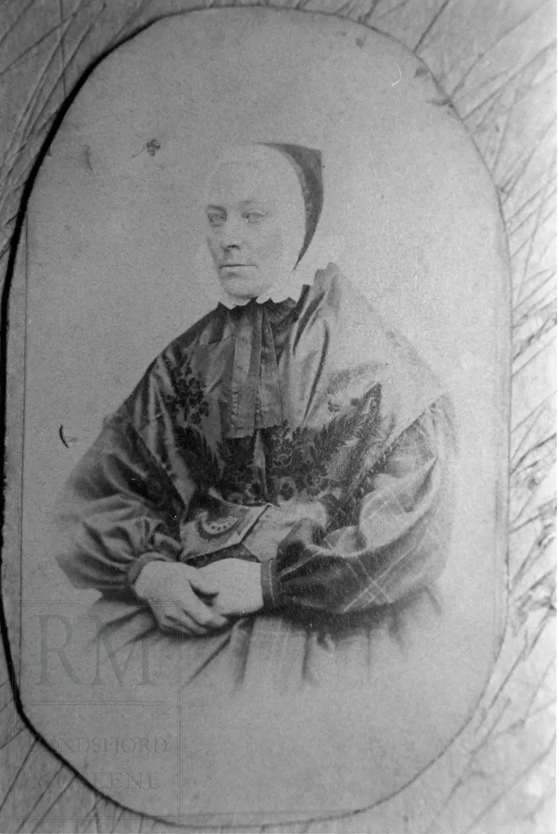 Portrett av Kari Olsdatter Hoff , gift Kari Haugtvedt (1822-1898), sittende i rutet kjole, honnlue med skru og med silkesjal over skuldrene.