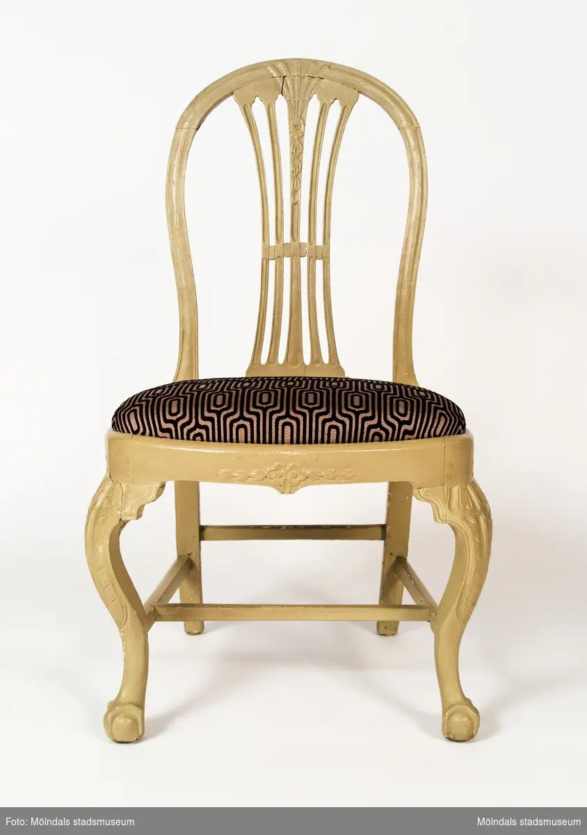 Axknippestol som kombinerar en gustaviansk rygg med ben utförda i rokoko. Stolen visar på ett intressant blandning där nya och gamla modeelement möts. Stolen är ej signerad men är utan tvivel tillverkad i Lindome.Stolen är ommålad 2002. Den grå färgen har lagts ovanpå den tidigare målningen, som var rosa och ljusblå och ornerad med guldfärg. Ommålningen har gjorts av Lars Olausson, möbelrenoverare.Stolen är inköpt år 2002 genom Per Falck, intendent vid Nordiska museet från antikhandlare Lars Broberg, Stockholm. 