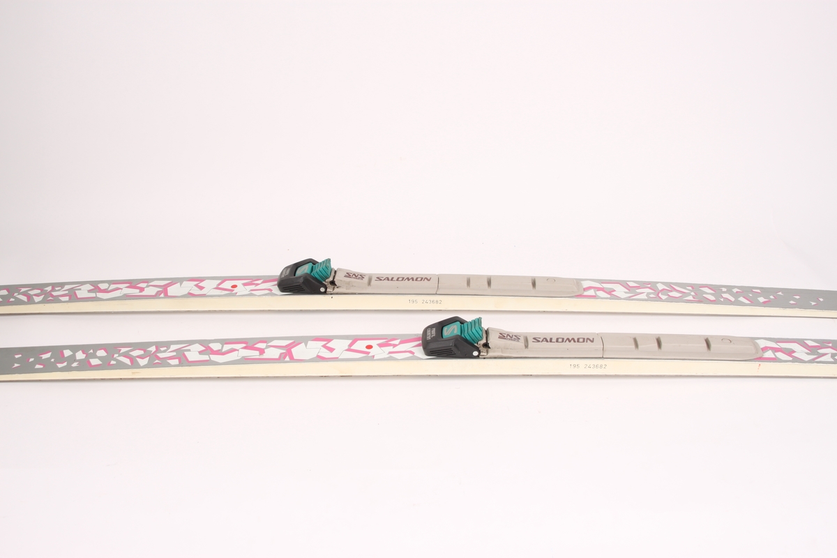 Et par ski med stålkanter og Salomon-binding. Til skiene er det festet en pose med to Salomon-bindinger.