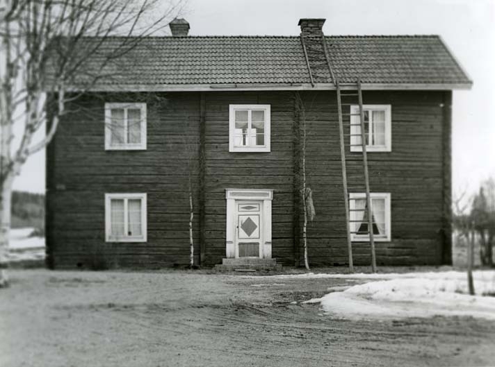 Boningshus med dörr dekorerad med rombmönster vid gården Hojars i Bjuråker. Framför huset står en kärve i trädgården och en stege lutad mot taket.