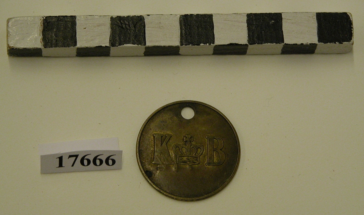 Rund bricka av mässing med ett stansat hål överst. På åtsidan finns det gjutet bokstäverna "K B" med en krona mellan.
Frånsida: stansat "E 114".