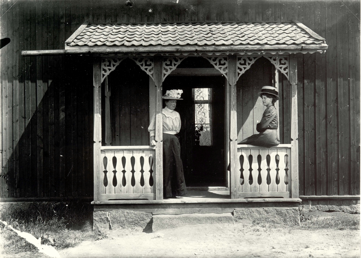Två kvinnor i för tiden typiska kläder på en veranda.