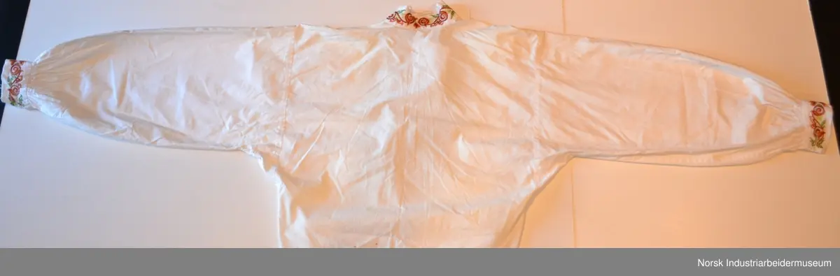 Plattsøm på kraven, mansjettene og bringa. Skjorten er åpen foran og helt ned.