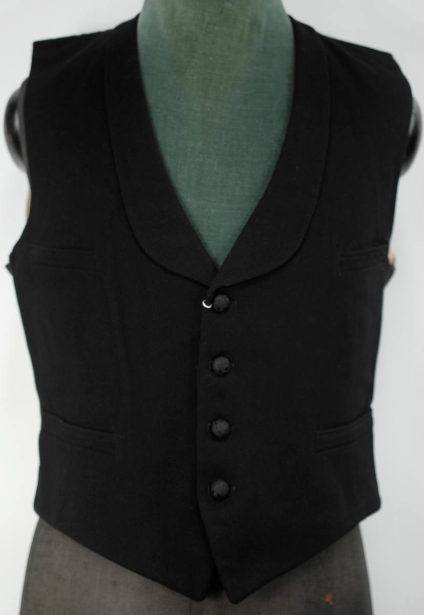 A: Jakke, Svart klede, krage med silkeslag. Enkeltspent, 1 trekt knapp, 3 trekte knapper på kvar arm. Svart silkefor. L.71,5 cm bredde ved skuldrane 45 cm
B: Bukse, svart klede, silkeripsbånd i sidene. L. 103 cm, Vidde nede 24 cm
C: Vest, svart klede, svart silkefor i rygg, foret med lystripet sateng. Enkeltspent med 4 trekte knapper, 4 lommer. L.48,5 cm x 38 cm
D: Sløyfe, Sort silkerips 55cm x 3,5 cm