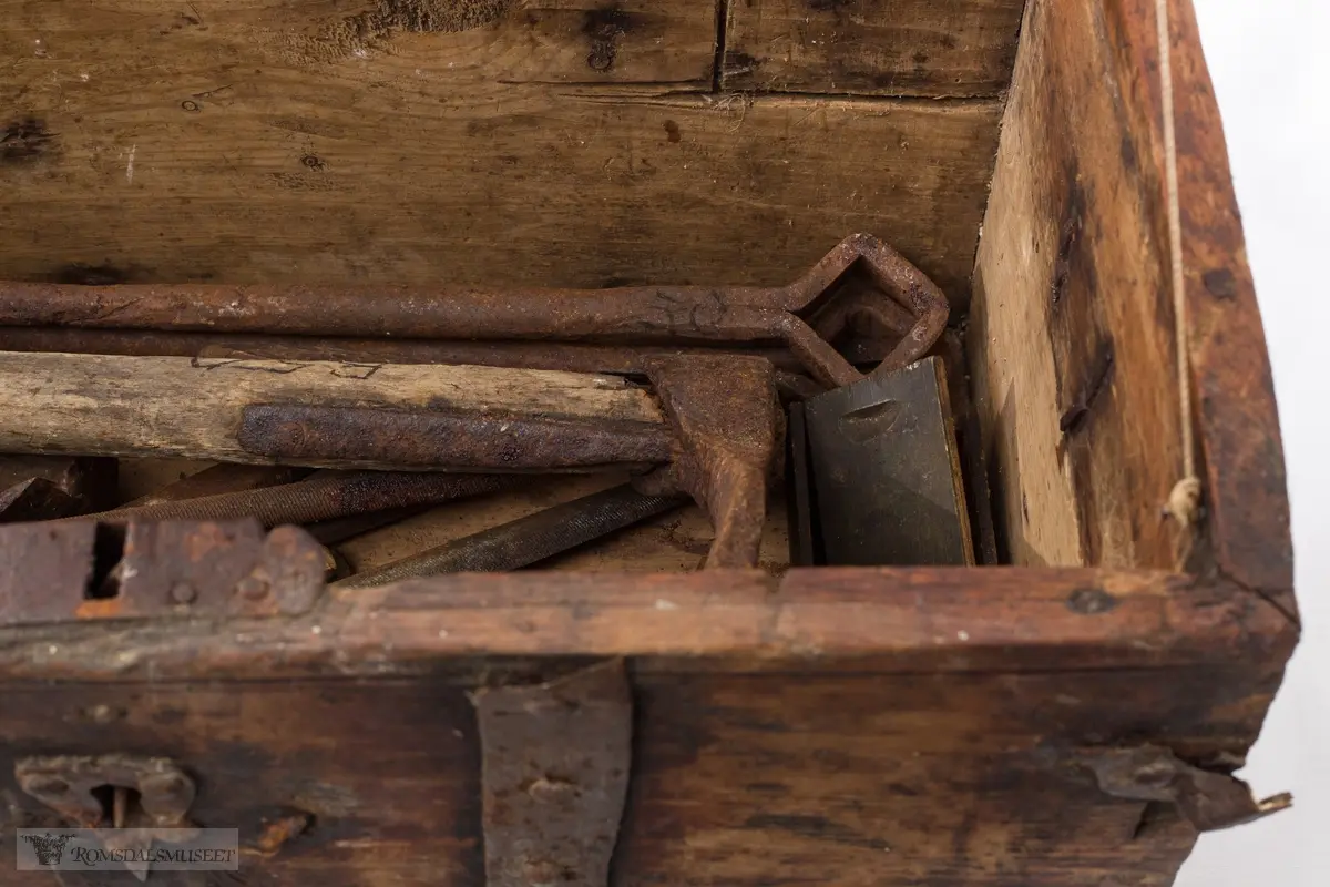 Rektangulær,jernbeslag og lås, svakt buet lokk. Inneholder diverse gammelt verktøy.