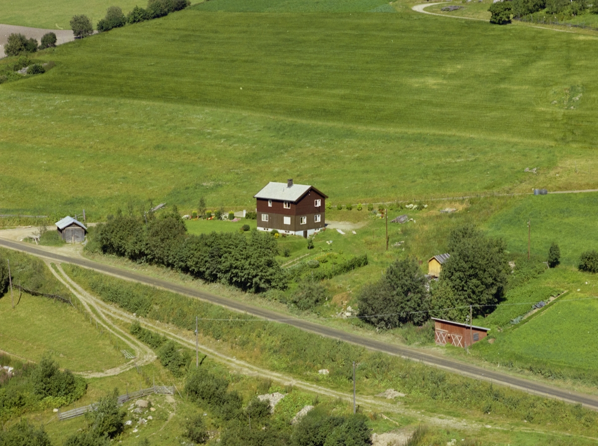 Hågå. Brunt to-etasjes hus med hage, utkant av åkerlandskap.