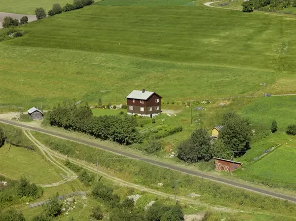 Hågå. Brunt to-etasjes hus med hage, utkant av åkerlandskap.