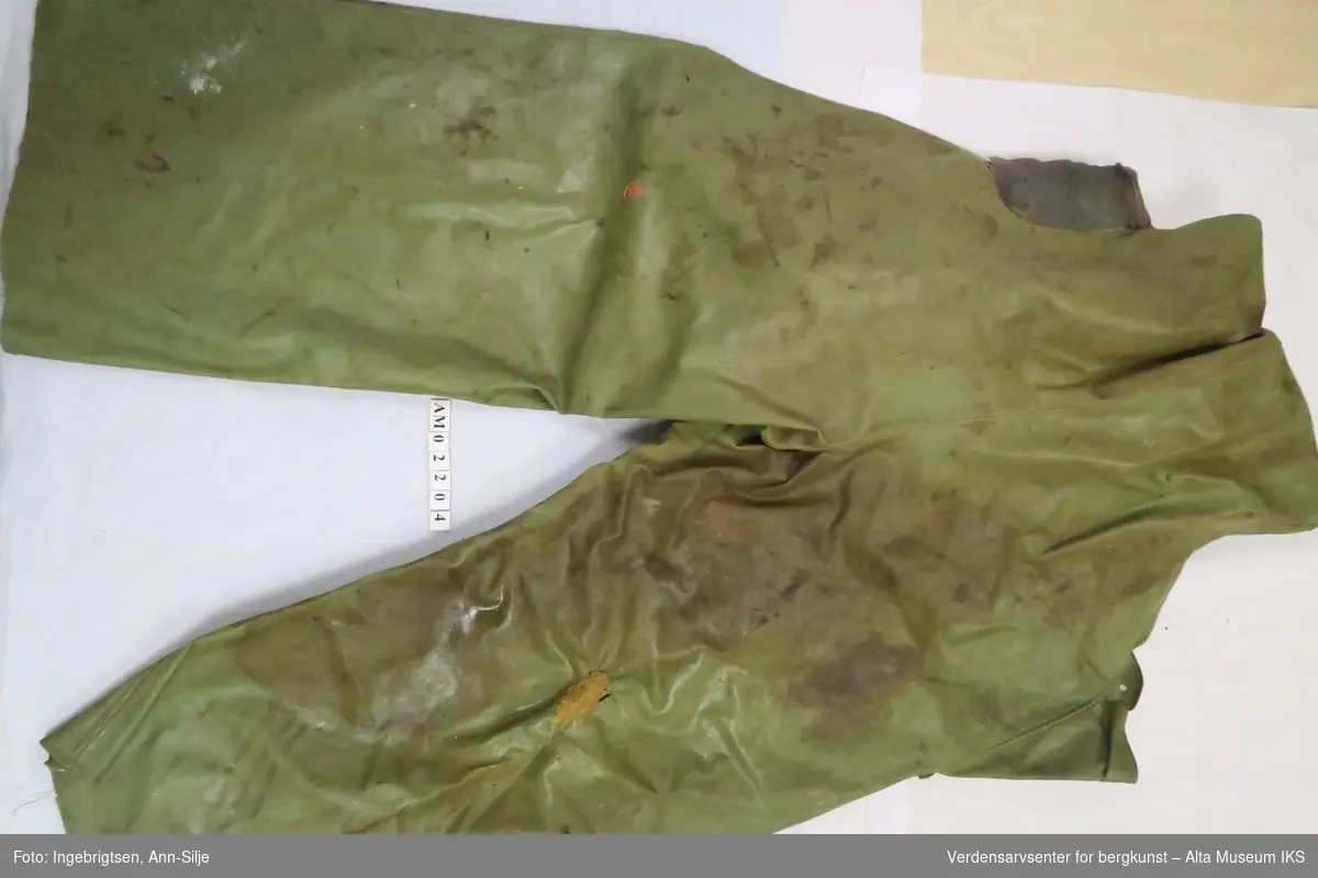 Grønn bukse med seler. Venstre bein er sydd med tråd av hamp i nedre del av ytre søm og et hull i låret.