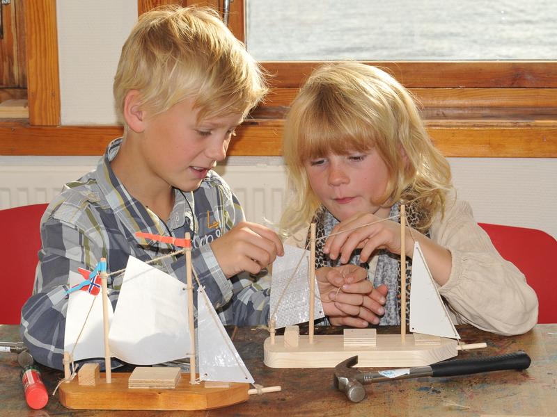 To barn i aksjon i Barnas båtverksted. Foran dem på bordet to lekebåter med seil, samt en hammer. (Foto/Photo)