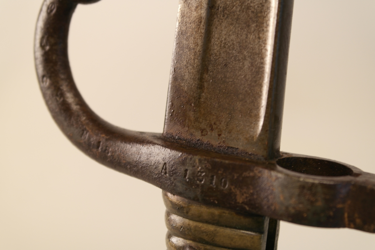 Bajonett (a) med slire (b). 
a) Støpt stål, smidd jern, messing. Stålklinge. Stopper av jern. Messinghåndtak med spor for geværet.
b) Jern.