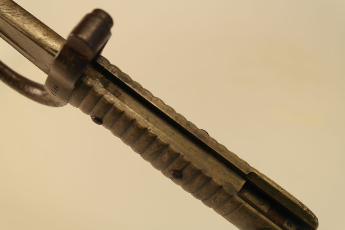 Bajonett (a) med slire (b). 
a) Støpt stål, smidd jern, messing. Stålklinge. Stopper av jern. Messinghåndtak med spor for geværet.
b) Jern.