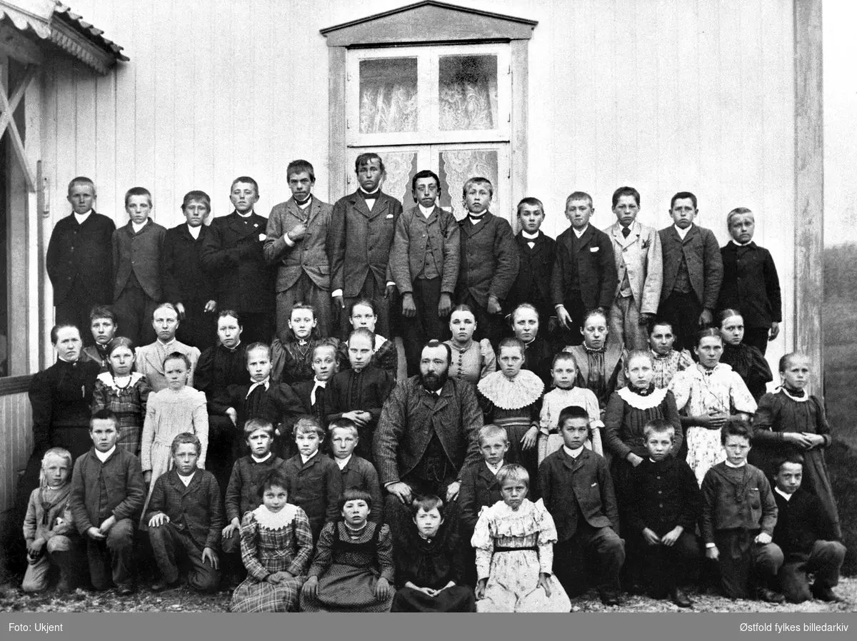 Jelsnes skole i Tune med lærer Strand og madam Tilla Strand 1895-96. Navneliste med plassering på bakside av fotokort %