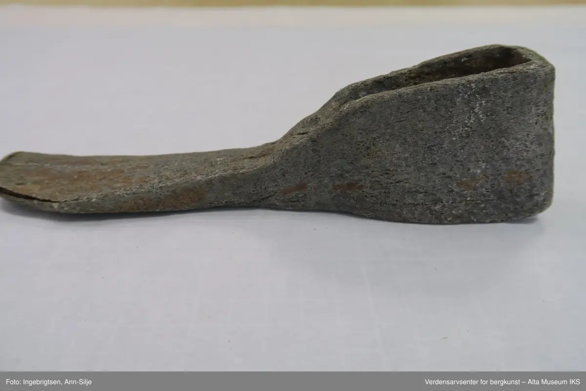 Hjemmesmidd jernhakke med innleggsstål. Jernet er brettet rundt skaftåpningen, det er lagt herdbart stål mellom. Hakken er hamret sammen (sveiset) på ambolt. I spissen er hakken stuket og sveiseskjøten er åpen både i spissen og fra skaftåpningen mot spissen. Dette tyder på mindre vellykket sveising, herding eller begge deler.