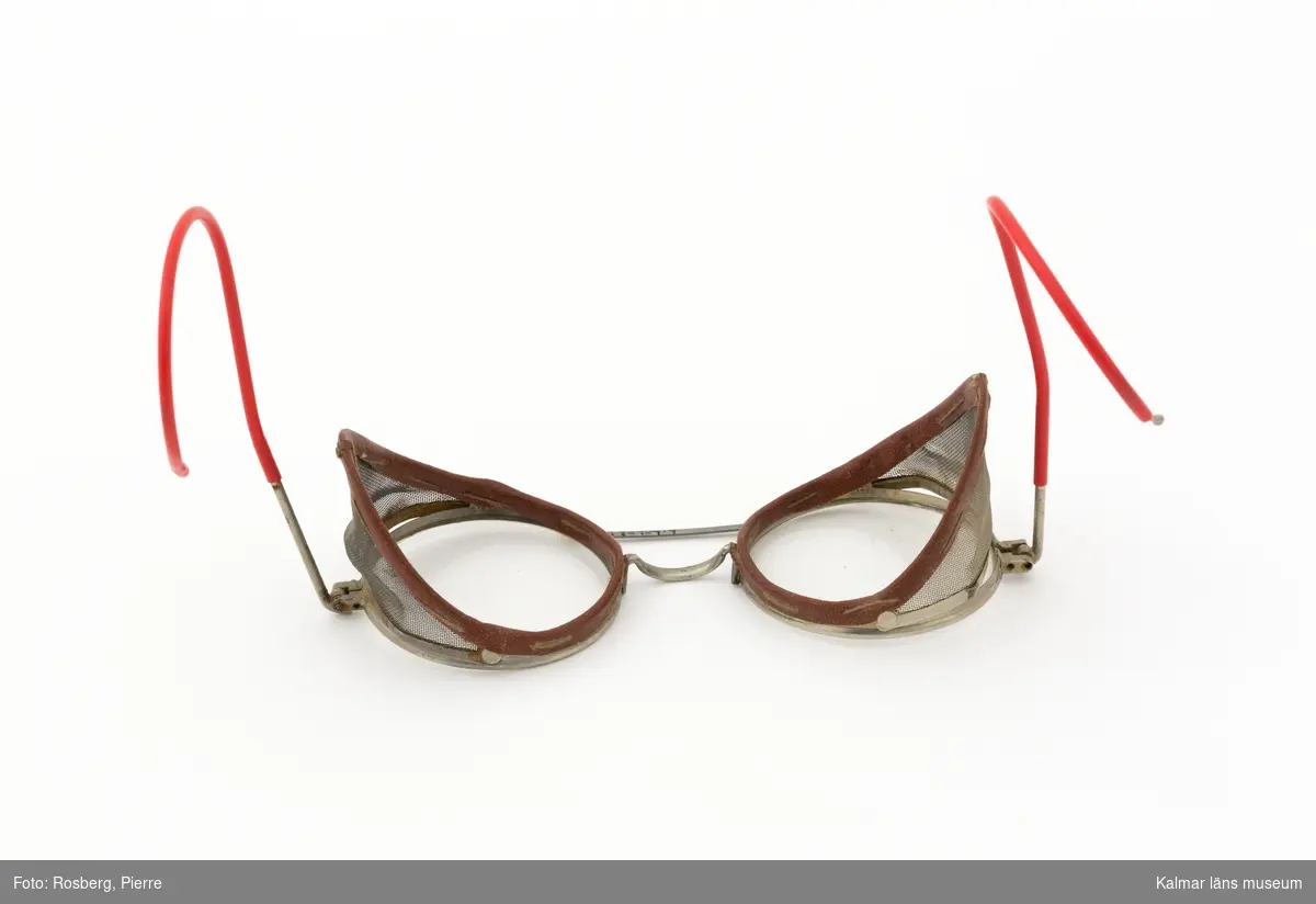 KLM 45909:9. Glasögon, skyddsglasögon. Runda glas, på sidorna nät av metall, för skydd. Bågar av röd plast.