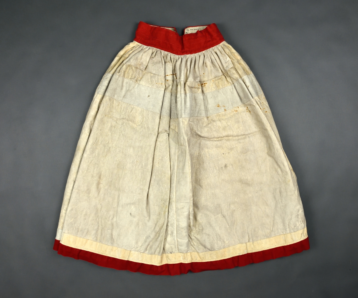 Kjol av svart och vitt fårskinn med hårsidan inåt. Kjolen är sydd i 4 våder med linning och list nertill av rött kläde.