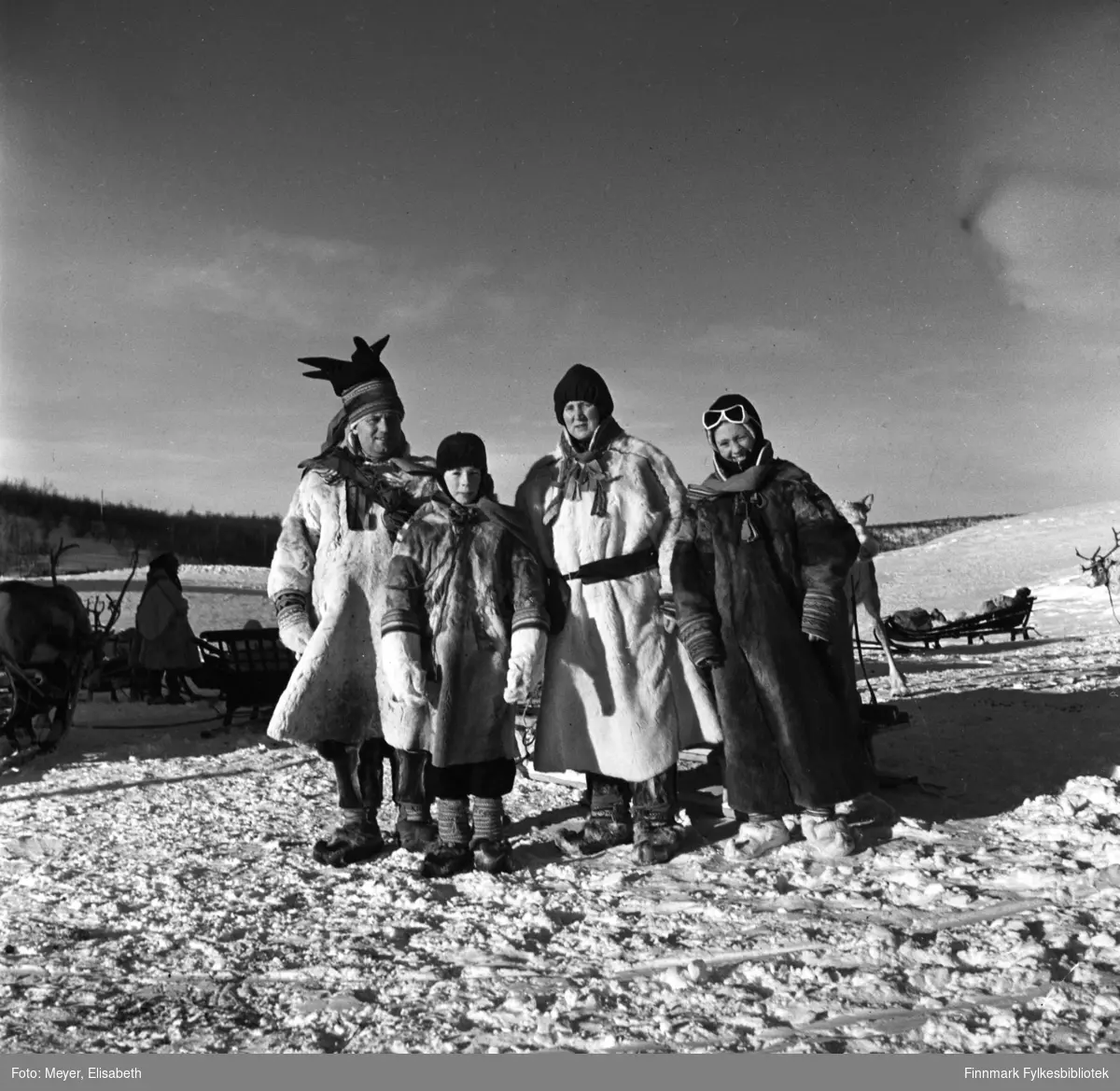Turister kledd i pesk besøker Statens fjellstue, Suolovuopm i Maze. Personer ukjente. Fotografert ved påsketider 1940. Suolovuopmi fjellstue ble etablert i 1843 og var den første som ble etablert i Finnmark. Etterspørselen etter overnattingssted i indre Finnmark kom da post og fogd skulle ut å reise. Fjellposten, som begynte i 1799 gikk fra Hammerfest til Haparanda om vinteren. Suolovuopmi Fjellstue ble brent under krigen i 1944 og ble så gjenoppbygd etter krigen - og er fortsatt i drift.
