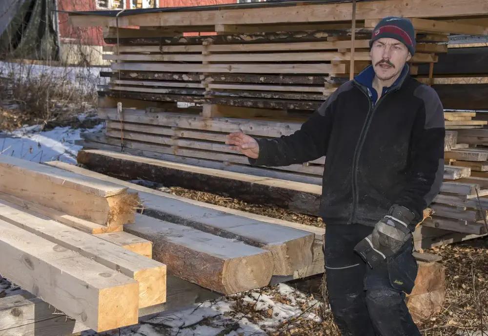 Tømrer står ved en plankestabel og forklarer hvordan de sagde plank i gamledager.