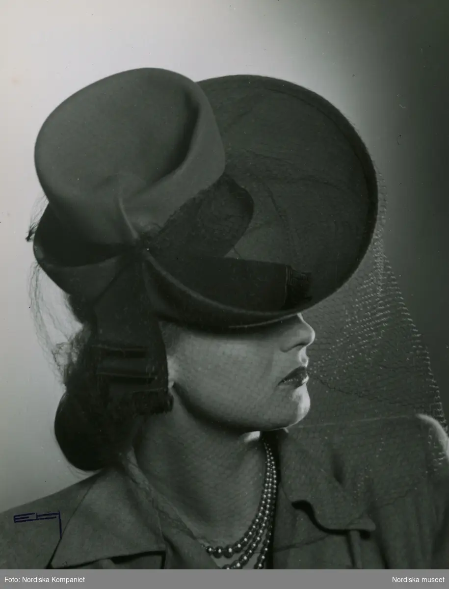 Modellen och skådespelerskan Hjördis Genberg  i hatt med kulle. Brättet uppvikt bak, rosett i ena sidan.