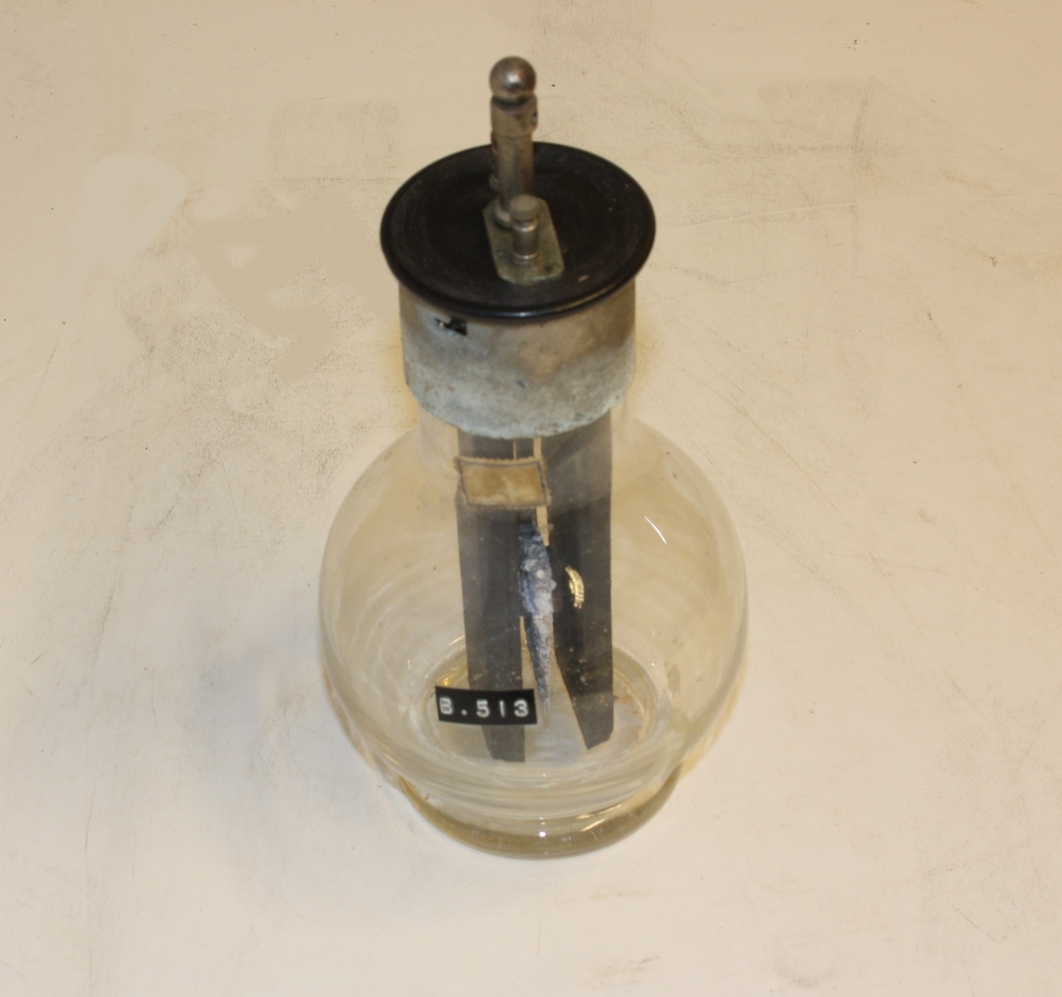 Kjegleforma kolbe/flaske med elektromagnet og tilkobling for strøm. Dette var nytta til å demonstrera korleis eit batteri virka.