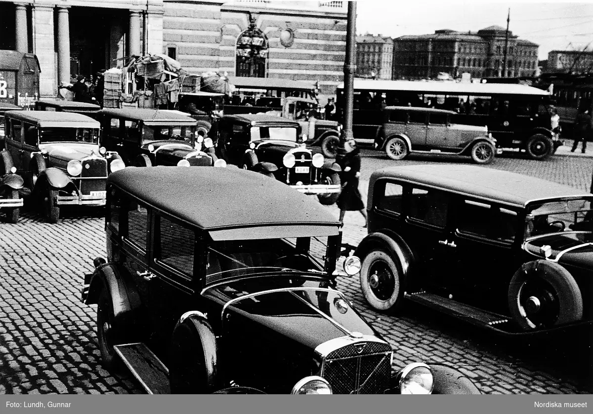Bilar parkerade på Gustav Adolfs torg vid Operan, Stockholm. Närmast står en Volvo PV 652 och bredvid står en Cord L29. I raden bakom ses från vänster: Stutz, Packard och Buick. I bakgrunden en buss.
