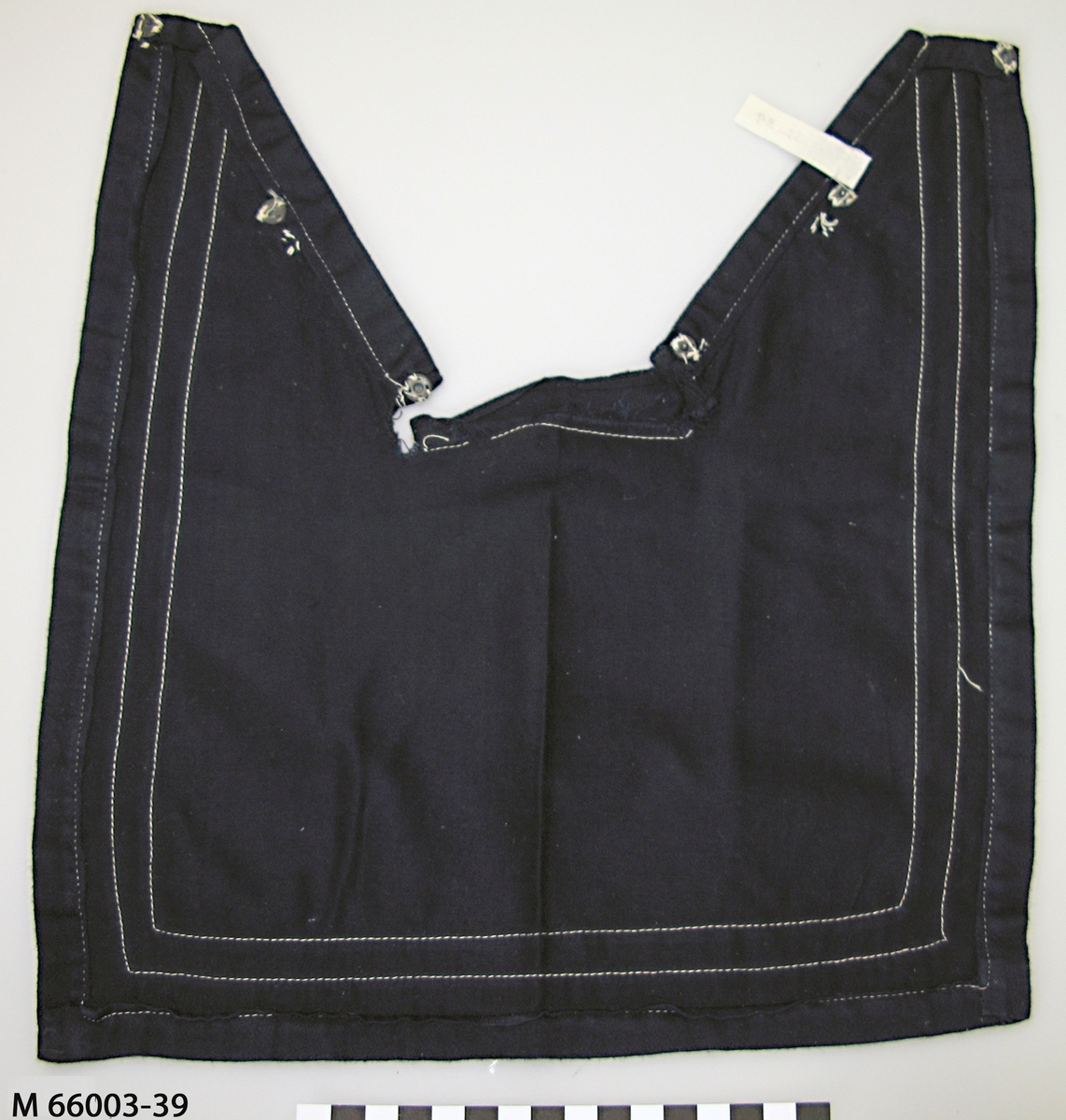 Mörkblå löskrage till sjömansskjorta i satinvävt bomullstyg dekorerad med tre vita flätade bomullsband fastsydda i de tre ytterkanterna. Två tryckknappar av metall i överkant på framsidan och sex på avigsidan för att fästa mot en skjorta.