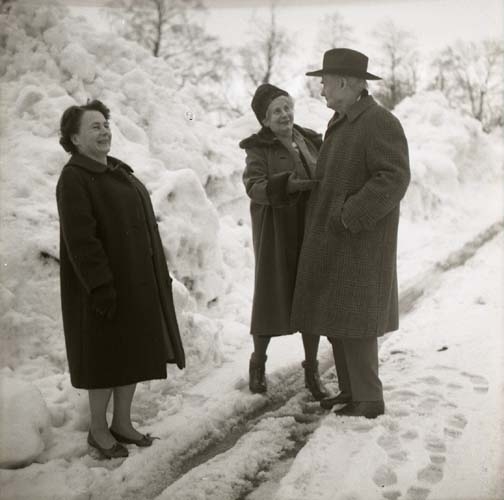 Två kvinnor och en man står vinterklädda på en väg den 8 april 1966. Ena kvinnan skrattar medan den andra pratar med mannen.