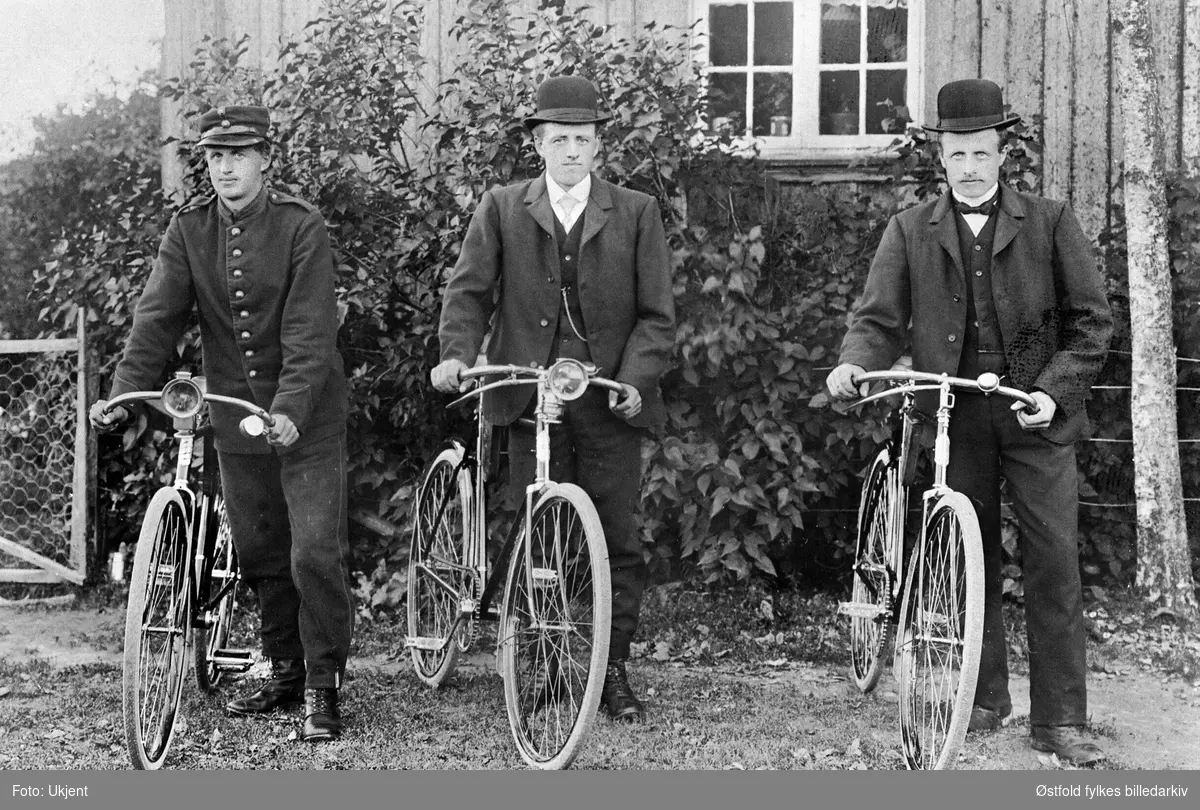 Postkort av tre herrer på sykkel utenfor våningshuset på Bøhler gård i Spydeberg. Fra venstre: Kristian Bøhler F.1893, Henrik Bøhler F. 1887, Johan Bøhler F.1884. Kristian har uniform. Guttene er brødre.
