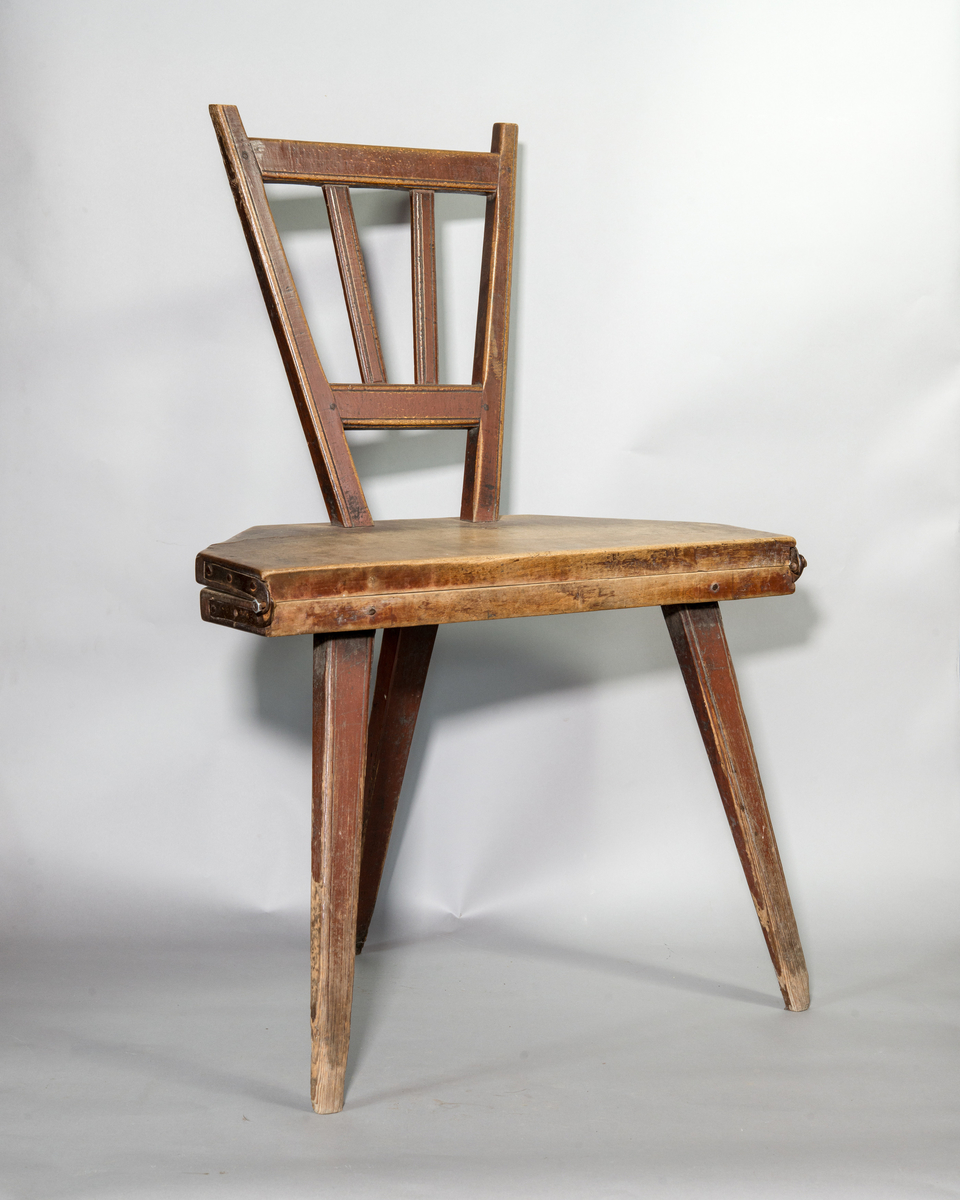 Bordsstol av trä, fällbar. 8-kantig sits i nedfällt läge. Rygg med tvärband och spjälor. Tre intappade ben och ryggen fungerar som fjärde ben i nedfällt läge. Gångjärn av järn. Rester av rödbrun och gul färg.