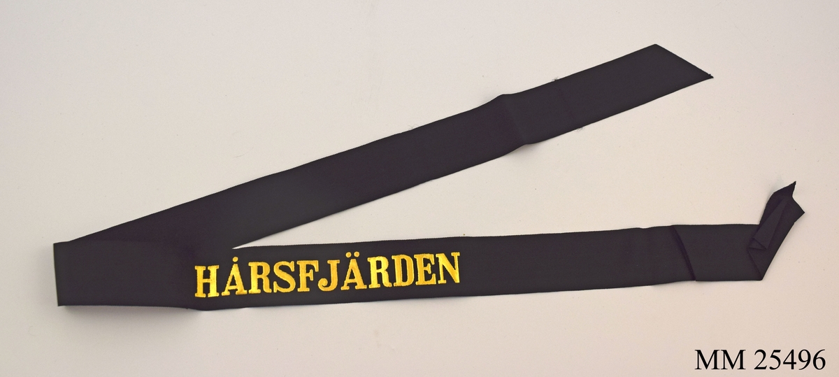 Mössband av svart sidenrips. Guldfärgad text med namnet "Hårsfjärden" på.