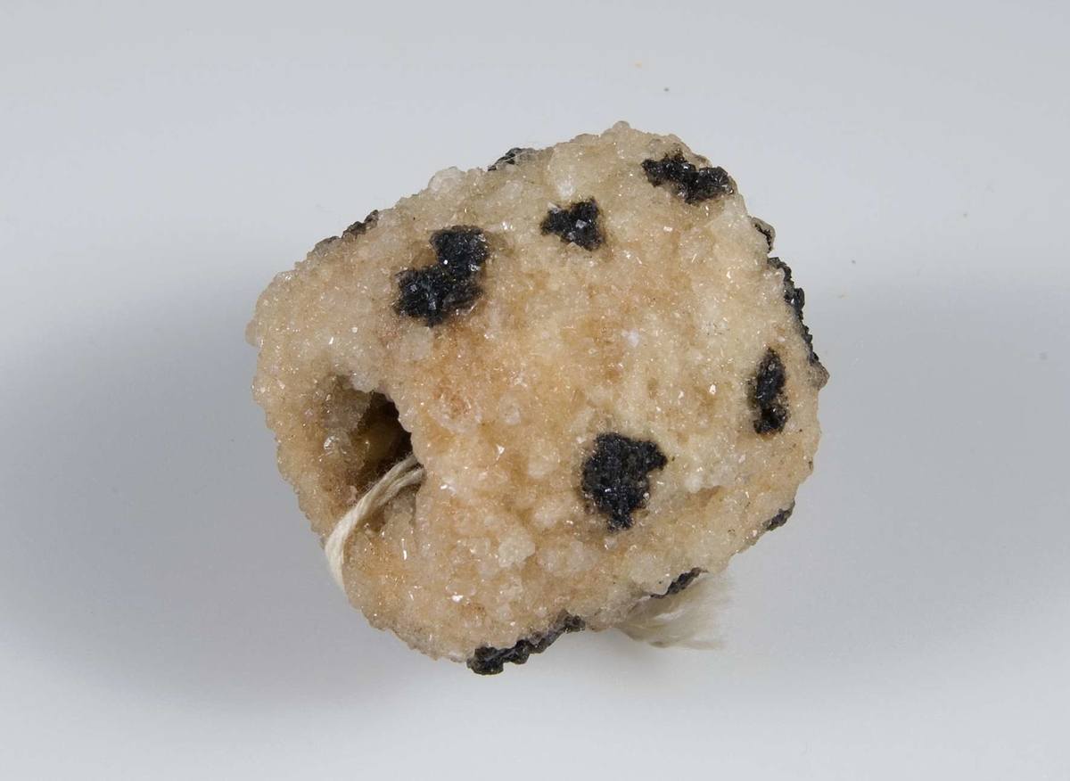Konfekt av sockermassa i form av en muff, vit med svarta prickar.Sammanhörande med konfekt UM16808-UM16 832.