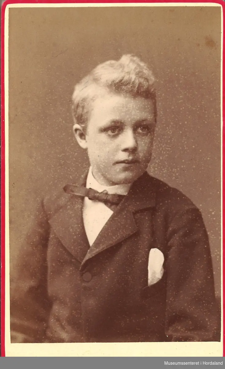 halvfigur fotografi av liten gut med jakke, kvit skjorte og slips