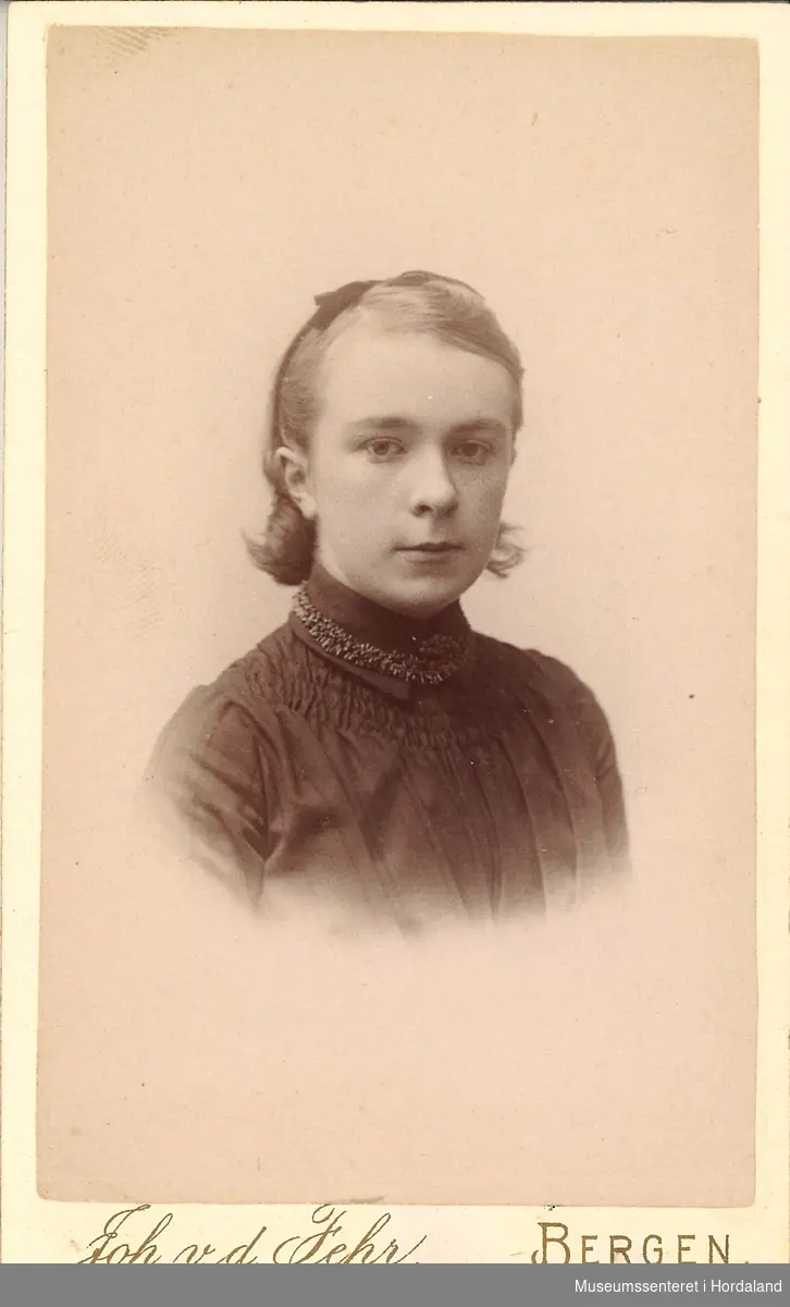 portrettfotografi av ung jente med hårband, mørk kjole og gimpa/strikka (?) band rundt halsen