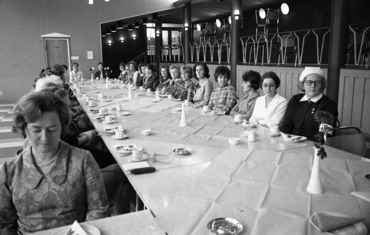 Tilstellning. Mange kvinner samlet rundt bordet, noen med armbind med rematisme-logoen. Taler.