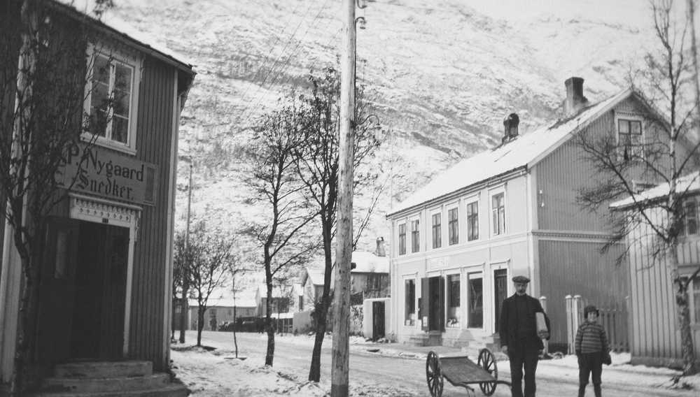 Seinhaustbilde fra petter Dass gate, Mosjøen, tatt mot vest og Øyfjellet.
I gata forfatteren Edvin Tverå og t.h. barnebarnet Erling, foran Skogs kolonial.