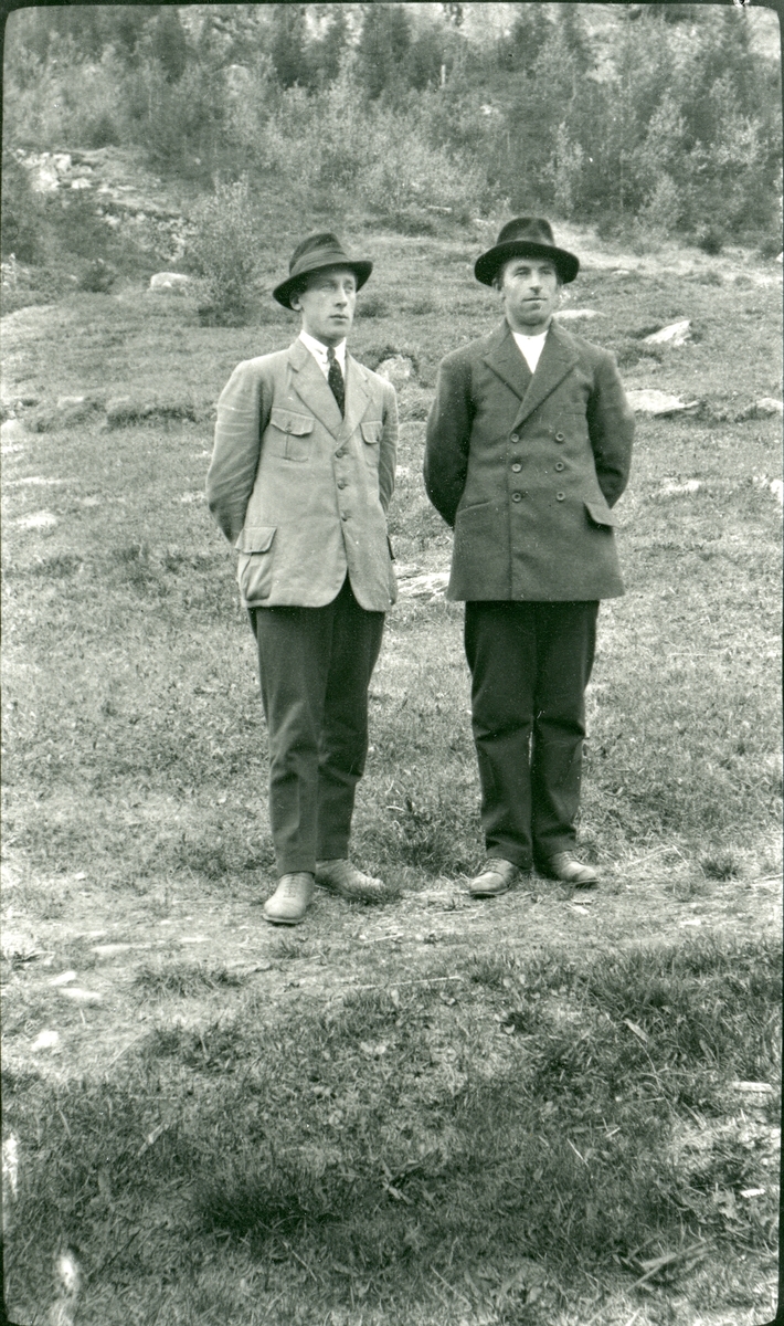 2 menn står på en sti i utmark. Begge har dressjakke, skjorte og slips.