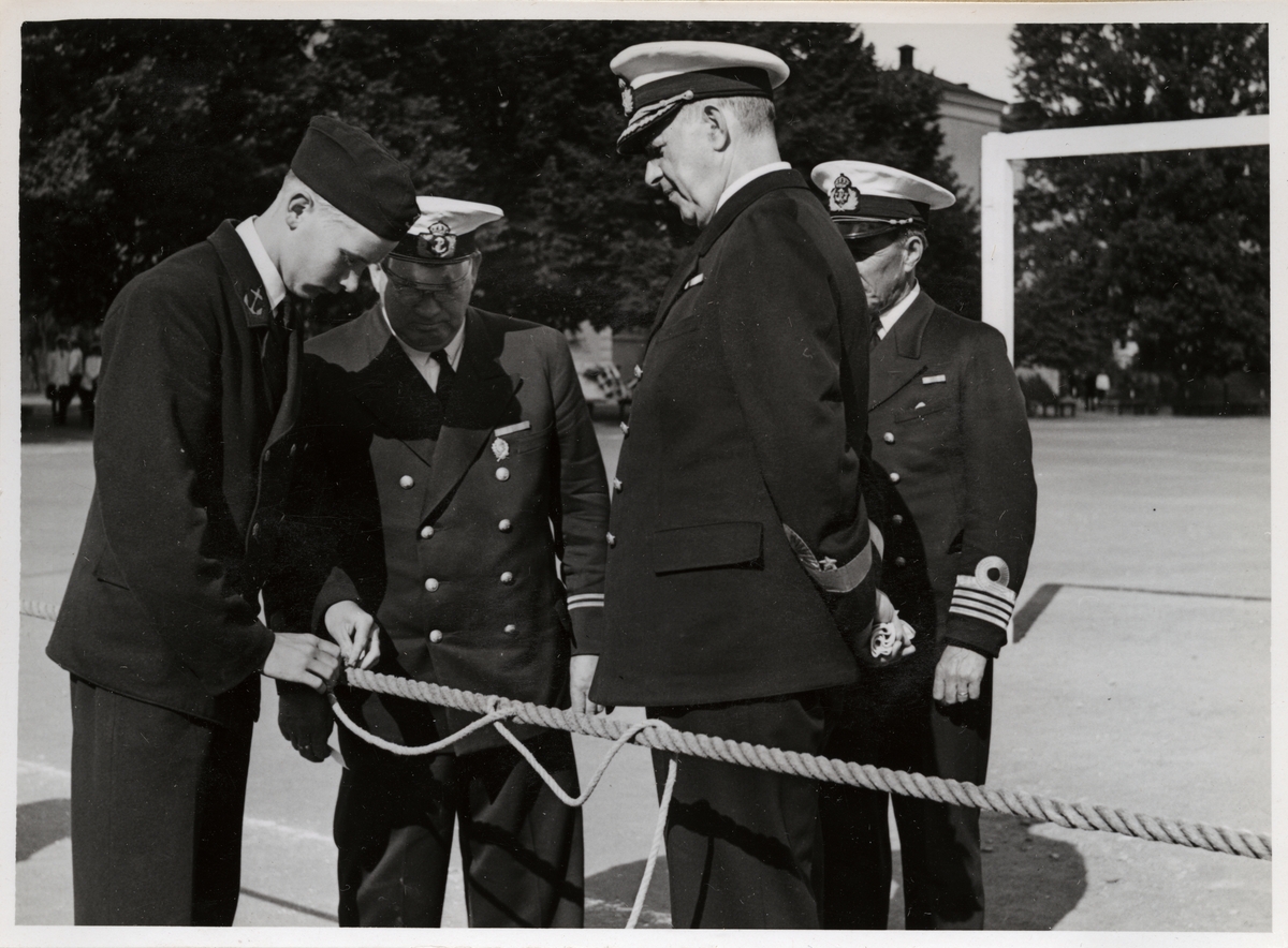 Bilden visar viceamiral Fabian Tamm tillsammans med flera officerskollegor som inspekterar hur en rekryt slår en stek runt en tampa.