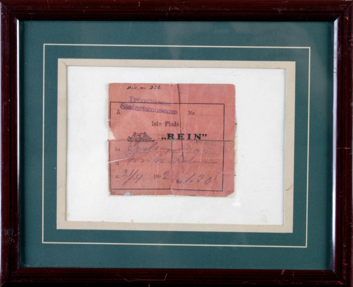 En billett fra båten D/S Rein som er rammet inn. Billetten er lys rød og har svart trykk samt at det er skrevet med blyant på, se "Påført tekst/merker". det er også trykt et lite bilde av en båt på billetten.  Det er en billett fra 1892. Den er montert på en papplate med et passpartout i grønt og hvitt. Rammen er en enkel treramme som er malt i en burgunderfarge. På baksiden er det en beige papplate festet med grønn papirtape. Opphenget er en enkel hempe laget av ståltråd som er festet oppe på rammen. Det er sekundær påskrift på baksiden, se "Påført tekst/merker".