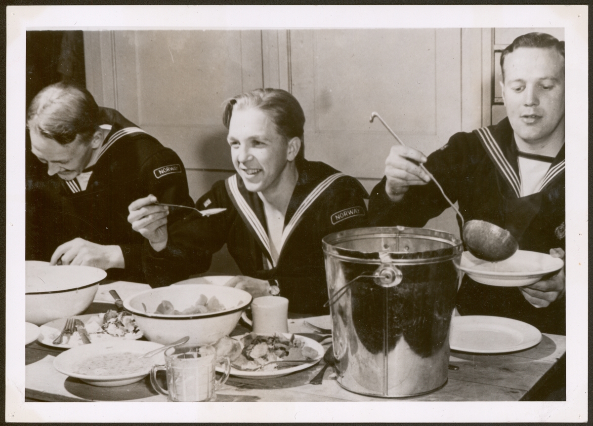 Tre norske soldater i marineuniformer ved matbordet.