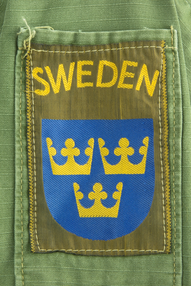 Vapenrock av modell m/61.  Vapenrocken är militärgrön och brukad vid FN-tjänst. Två bröstfickor fram med dold knäppning. Dold knäppning fram med synlig övre knapp vid halsringning. Slejf på vardera axel för axelklaffhylsor. På vänster axel (framifrån) sitter ett ljusblått tygmärke med FN logga, på höger axel sitter ett tygmärke med Svensk vapensköld och texten "SWEDEN" i gult. Storlek Medium/Regular.