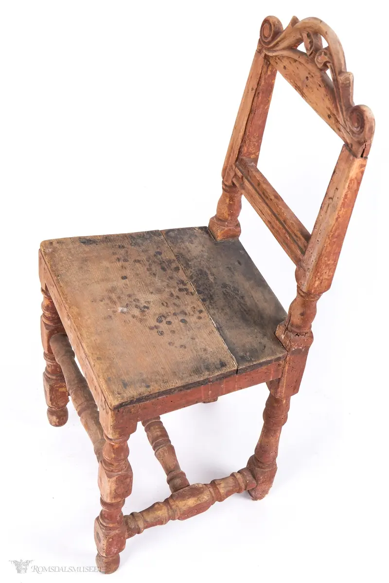 Krone med symmetrisk utskåret motiv. Volutter på sidene og et organisk motiv i midten.